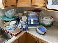 Countertop filled with assorted plastic containers, glass bowls, Corning Ware dishes and funnels