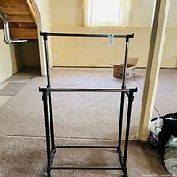 Front view of two-tier black metal clothing rack in room