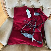 Burgundy electric heated throw folded on chair with controller and power cord visible