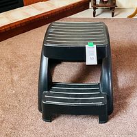 Front view of black two-step plastic stool on carpet