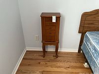 Front view of closed wood jewelry armoire chest showing drawers and legs