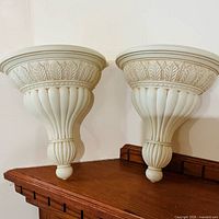 Front view of two matching off-white acanthus leaf wall sconce shelves