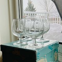 Four clear etched brandy snifters on box near window