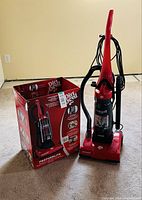 Upright vacuum beside its original box on carpeted floor