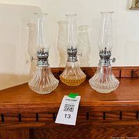 Three clear glass Lamplight Farms kerosene oil lamps on mantel
