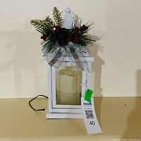 Full view white metal lantern with decorative greenery and attached MaxSold tag