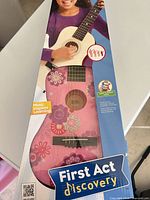 Retail box front showing First Act Discovery pink floral guitar and accessory callouts