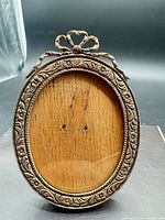 Front view of oval .800 silver frame with floral border and bow crest