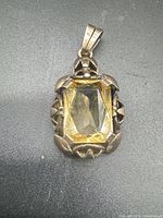 Front view of pendant showing yellow faceted stone and decorative gold setting