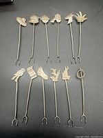 All 12 sterling silver picks laid out showing different finials and two-prong ends
