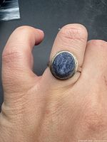 Ring on hand showing bezel-set blue stone and band profile