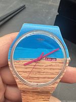 Front view of Swatch watch showing beach scene dial and hands