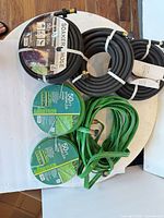Overall view of three coiled black soaker hoses and three green flat sprinkler hoses with packaging