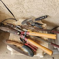 cluster of hand garden tools including shears, trowels, pruning saw
