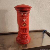 Front view of red ceramic Japanese post box coin bank showing coin slot, kanji, postal emblem, and molded base