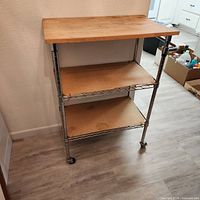Front view showing wood top, two wire shelves, chrome frame and casters