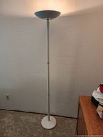 Full view of illuminated white torchiere floor lamp against wall