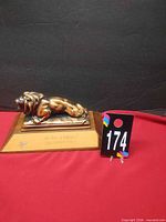 Front view of brass lion trophy on wooden base with lot tag