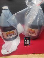 Two Demco black paint jugs side by side, one wrapped in plastic, lot tag visible