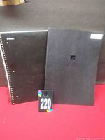 Two black graph paper notebooks, one Mead spiral-bound, one black glue-bound, on red background