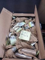 Open box filled with multiple tan jute curtain tassels, tags visible