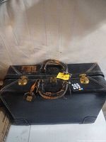 Front view of black suitcase showing brass latches, handle and overall wear