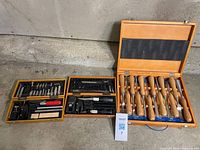 All three wooden tool cases opened showing contents: chisel set on right, two accessory tool sets on left