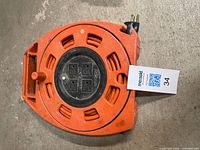 Full view of orange NOMA cord reel showing handle, reel body, and attached plug