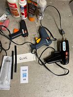 Three glue guns, bottled glues and glue sticks on concrete surface