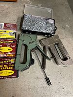View of both staple guns, plastic organizer of brad nails, Arrow T50 staples packaging and pry tool
