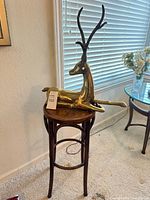 Full view of brass deer sculpture resting on stand