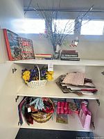 Cabinet showing books, faux floral vase, white basket with artificial flowers, stationery stack and gift bags