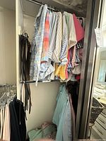 Closet section with upper rod of multiple women’s shirts/blouses, lower belts and folded garments