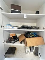 Cabinet shelves showing entire lot: electronics on upper shelves, box of cables, granite tiles on bottom