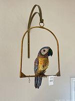 Full view of enamel parrot on brass swing hanging from wall bracket