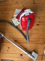 Overall view of red canister vacuum with hose, wand, floor head and vacuum bag pack