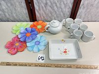 Group shot of baker, teapot, six mugs and six flower plates