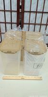 Four sealed plastic canisters with beige lids beside ruler, showing height approx 9 in