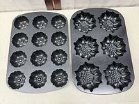 Top view of both black Nordic Ware pans, 12-cavity fluted flower pan on left, 6-cavity sunflower pan on right