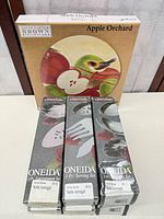Three Oneida Satin Astragal boxed flatware sets front view with Sakura Apple Orchard trivet box in background