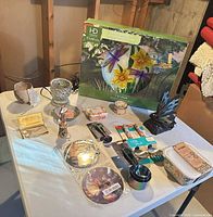 Entire lot on table showing boxed birdbath, butterfly lamp, utensils, décor items, container