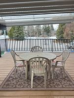 Full patio set on deck showing table, four chairs with cushions and rug