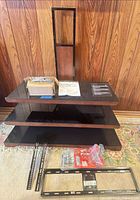 Partially assembled stand showing three glass shelves, wood support, hardware box, manual and mounting components.
