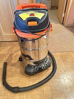 Front view of Kubota stainless steel wet/dry vacuum with attached hose and castor base