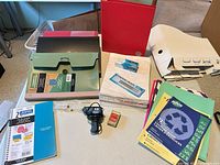 Overview of folders, notebooks, paper packs, glue gun, staples, thumb tacks on table