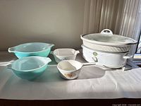 Group shot showing slow cooker, two turquoise Pyrex bowls, CorningWare casserole, fruit motif saucepan