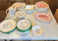 Overview of dinnerware on table: red plates stack, blue folk plates, teapot, beige plates, cream bowl