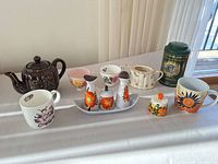 Group shot of all teaware, condiment pieces, mugs and tin