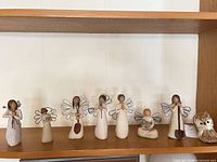 All seven angel figurines and straw owl arranged on shelf