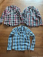 Group shot of all three plaid flannel shirts laid flat